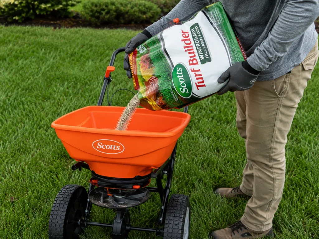 Professional filling a broadcast spreader with Scotts Turf Builder fertilizer to apply on a green lawn