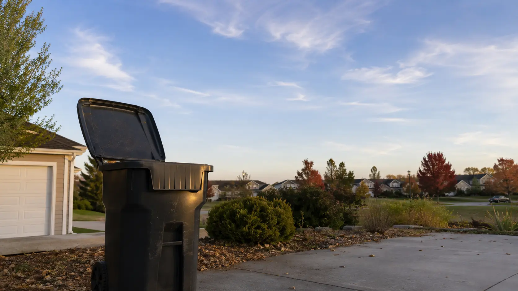 Open residential trash bin on suburban driveway causing a maggot infestation.